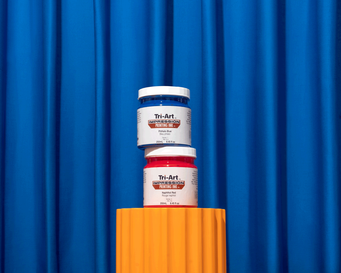 This is a gif of two jars of impressions acrylic printing ink. A hand comes from out of frame to grab one.