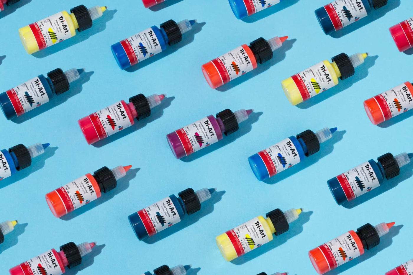 This is a flat lay image of a bunch of bottles of Tri-Art Low Viscosity acrylics.
